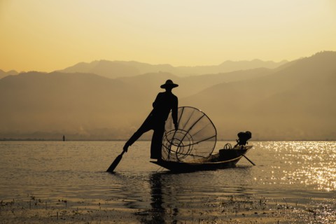 Asian fisherman rowing canoe on rural lake