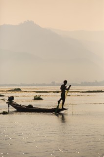 Asian fisherman rowing canoe on rural lake