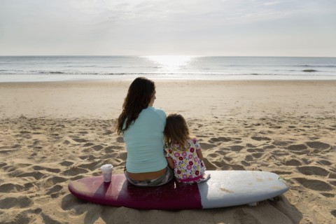 Mother and daughter sitting on surfboard at beach