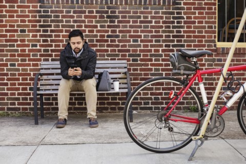 Hispanic man sitting on city bench using cell phone