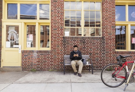 Hispanic man sitting on city bench using cell phone