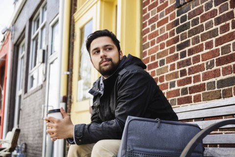 Hispanic man sitting on city bench drinking coffee