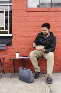 Hispanic man eating bowl of food on sidewalk