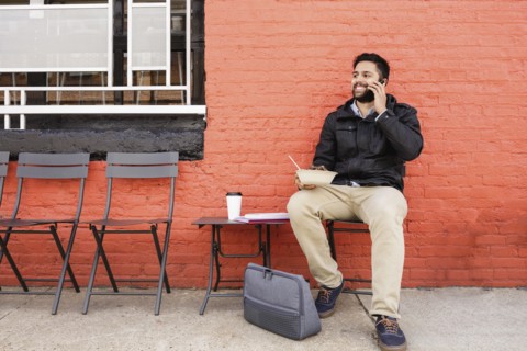 Hispanic man eating bowl of food on sidewalk using cell phone