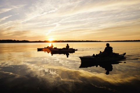 Silhouette of people fly fishing in kayaks on river