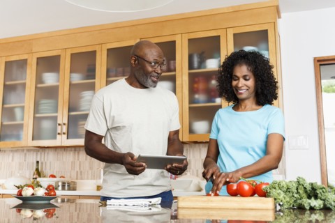 Black couple with digital tablet chopping tomatoes in kitchen
