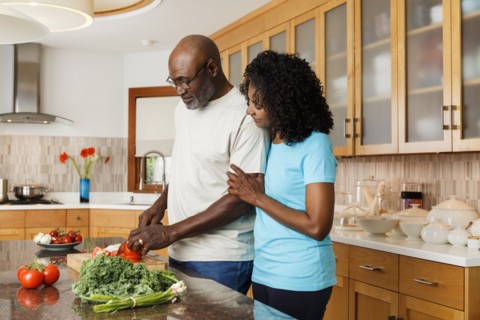 Black couple chopping vegetables in kitchen
