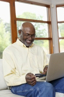 Black man online shopping with credit card and laptop on sofa