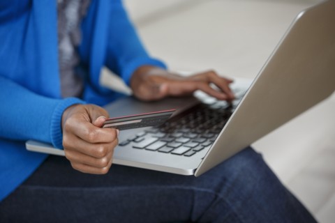 Black woman online shopping with credit card and laptop on sofa