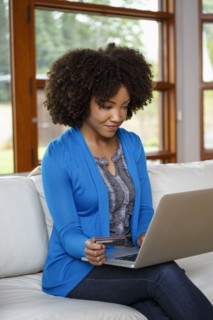 Black woman online shopping with credit card and laptop on sofa