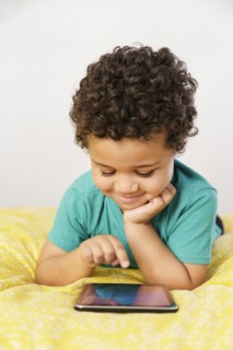 Smiling Mixed Race boy laying on bed using digital tablet