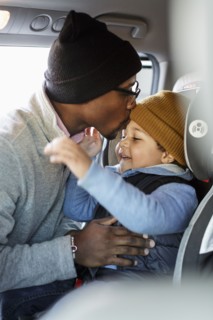 Father kissing son in car seat on forehead