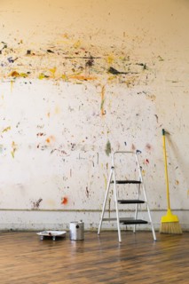 Paint splattered on wall near ladder and broom