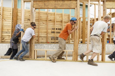 Volunteers pushing framed wall at construction site