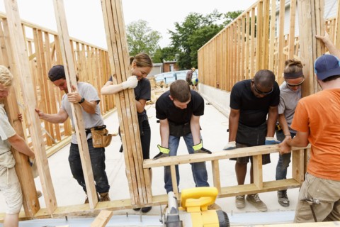 Volunteers lifting framed wall at construction site