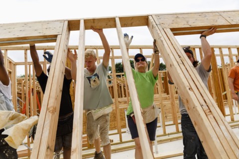 Volunteers lifting framed wall at construction site