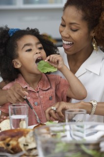 Young girl eating a leaf of lettuce at the dinner table