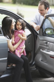 Hispanic mother and daughter sitting in car with door open talking to father