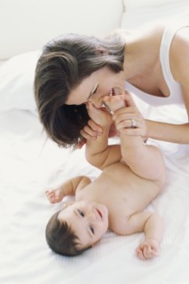 Mother kissing baby's feet on bed