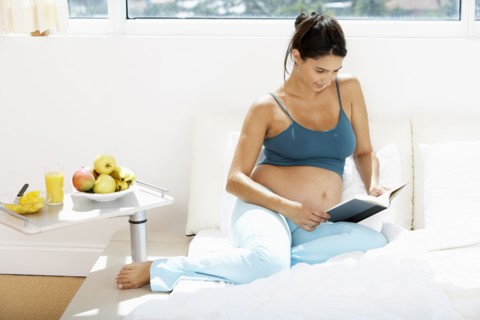 Pregnant Hispanic woman reading in bed