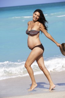 Pregnant Hispanic woman walking on beach