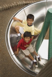 Asian boys sliding down circular slide