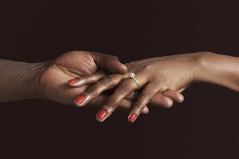 African woman with engagement ring holding fiancee's hand
