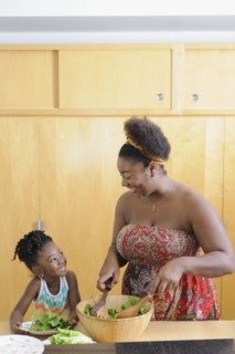 Black girl with mother preparing salad in kitchen