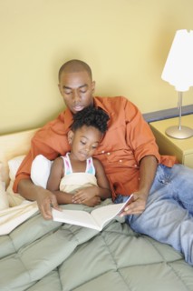 Black father reading book to daughter in bedroom
