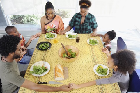 Black family saying grace at dining room table