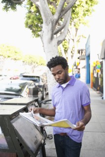 African American man reading newspaper on sidewalk