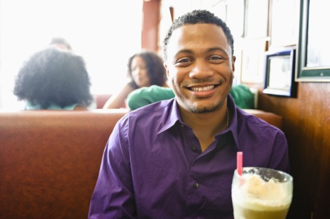 Smiling mixed race man with milkshake in diner booth