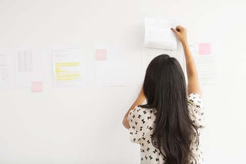 Businesswoman taping up papers on office wall