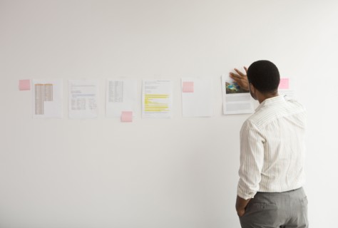 Black businessman taping up papers on office wall