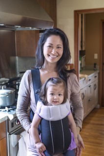 Mother holding daughter in sling in kitchen