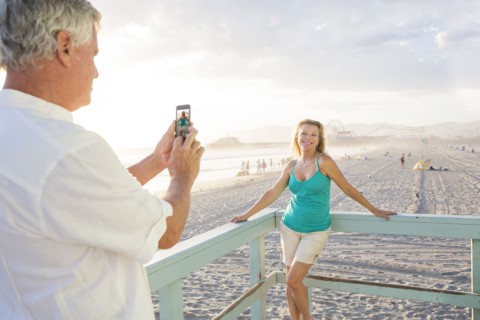Caucasian man taking photograph of wife on boardwalk at beach