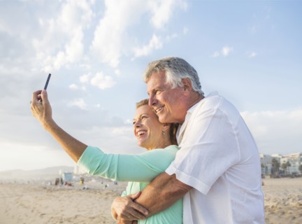 Caucasian couple taking cell phone selfie on beach