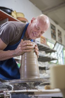Older Caucasian man forming pottery on wheel in ceramics studio