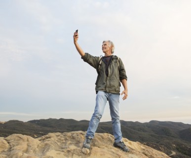 Older Caucasian man taking cell phone photograph on rocky hilltop