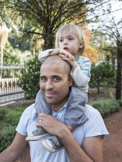 Hispanic father carrying son on shoulders in park