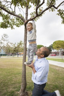 Hispanic father and son playing on tree in park