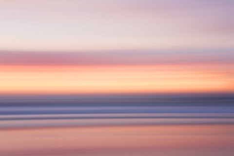 Defocused view of ocean waves on beach under sunset sky