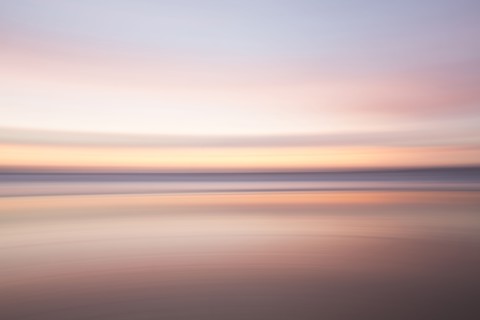 Defocused view of ocean waves on beach under sunset sky