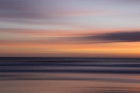 Defocused view of ocean waves on beach under sunset sky