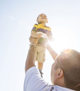 Low angle view of Hispanic father lifting son in air
