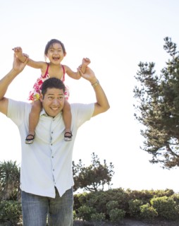 Hispanic father carrying daughter on shoulders