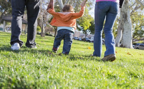Hispanic mother and father helping son walk in park