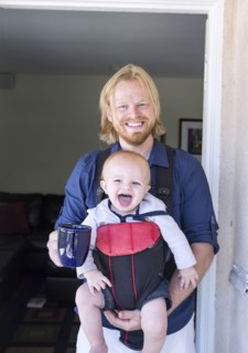 Caucasian father wearing son in harness in doorway