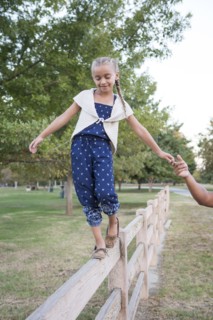 Father helping daughter balance on wooden fence