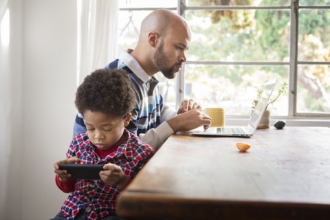 Mixed race father and son using technology at table